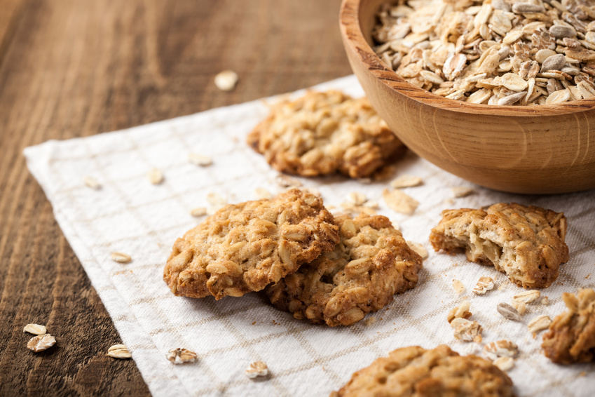 Homemade oatmeal cookies and oat flakes on white cloth napkin with wooden tabletop background