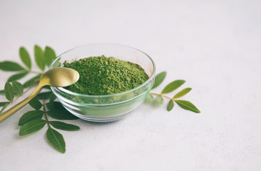 glass bowl filled with fresh chlorophyll powder. A gold spoon rests on the bowl's edge