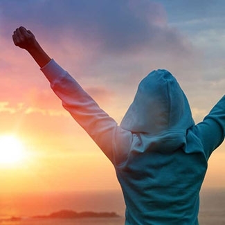 Person with arms raised in front of sunset